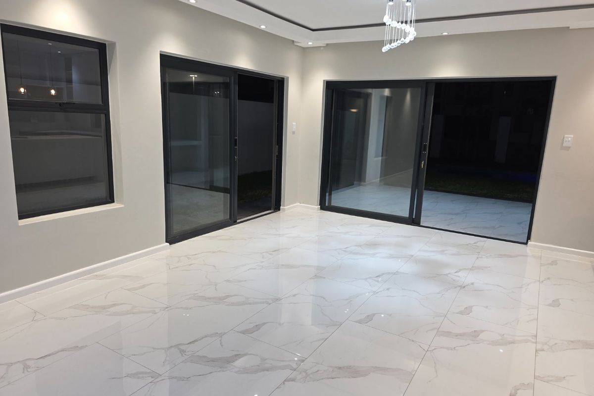 Spacious, modern living area featuring high-gloss marble-look floor tiles, recessed ceiling lighting, and large black aluminium sliding doors leading to the exterior.