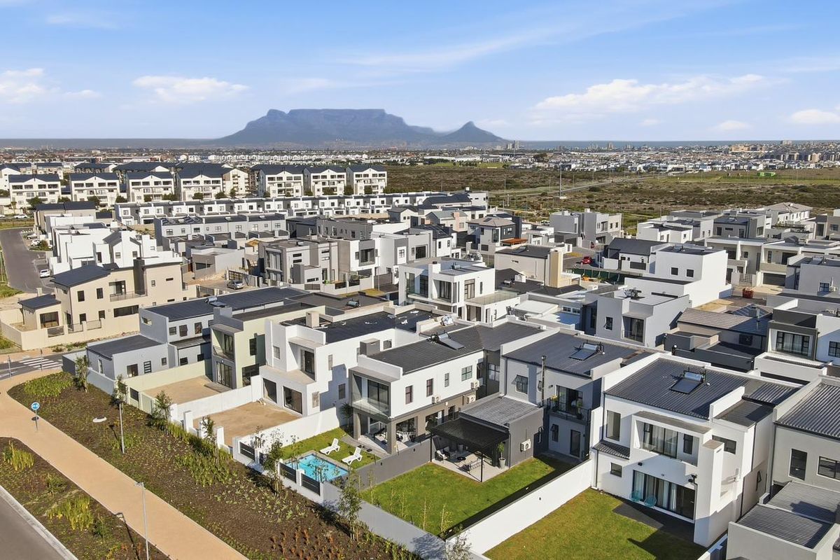 An aerial view of a modern residential estate featuring contemporary homes, private gardens, swimming pools, and solar installations with a mountain backdrop.