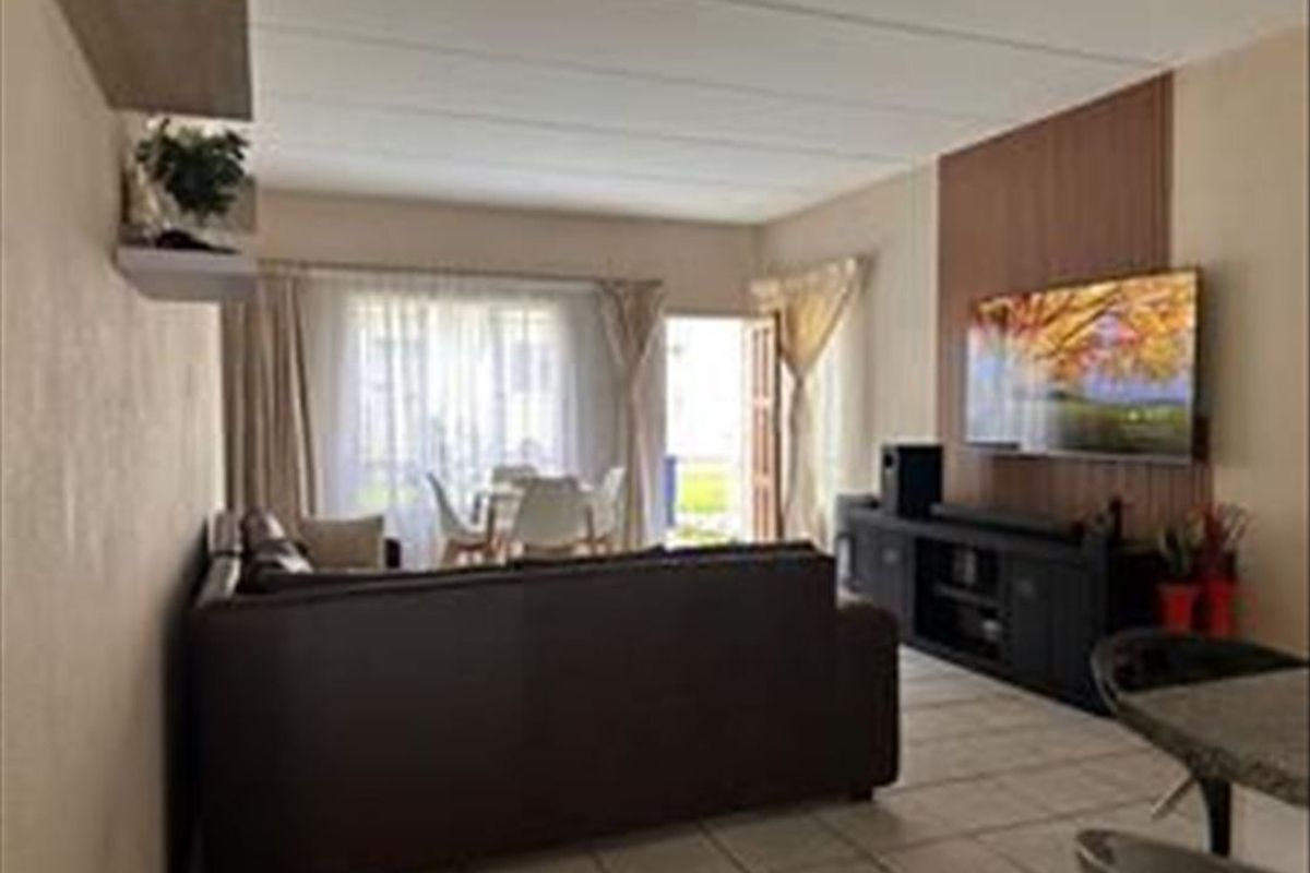 A living room featuring tiled flooring, wood-look accent wall paneling, and a sliding glass door providing access to the outdoor area.