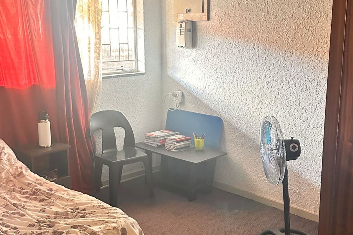 A bedroom featuring textured walls, a pendant light fixture, and a window with security bars. The space requires cosmetic updates to improve its appeal.