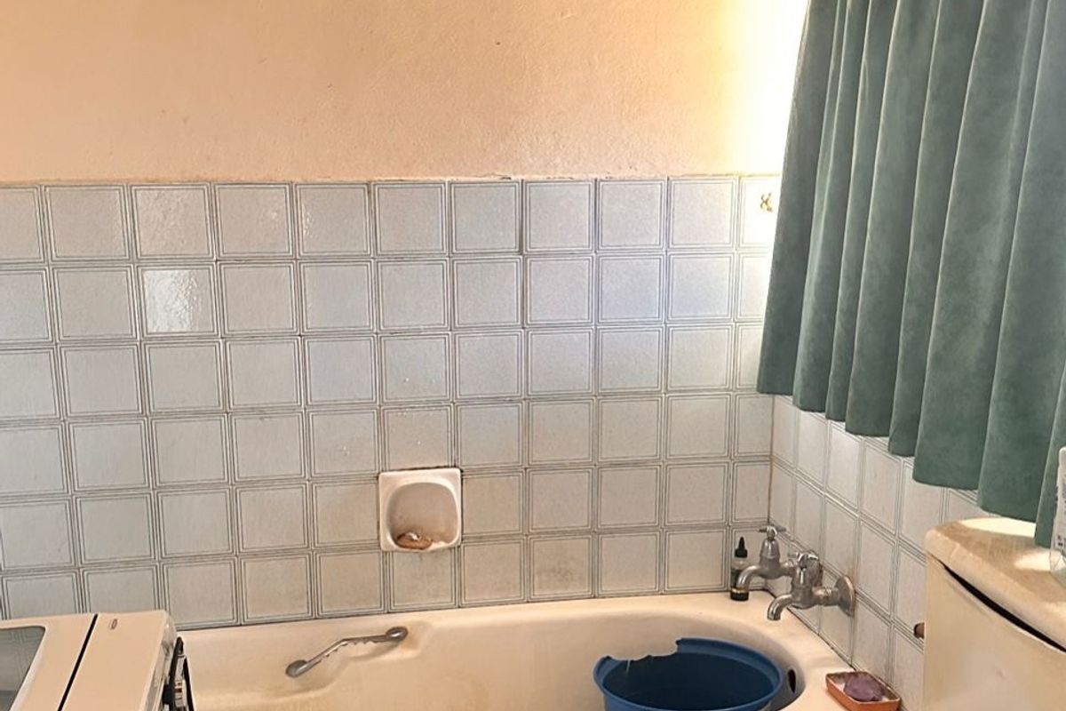 A dated bathroom featuring a built-in bathtub, ceramic tiling, and standard toilet. The space requires renovation to update finishes and improve overall condition.
