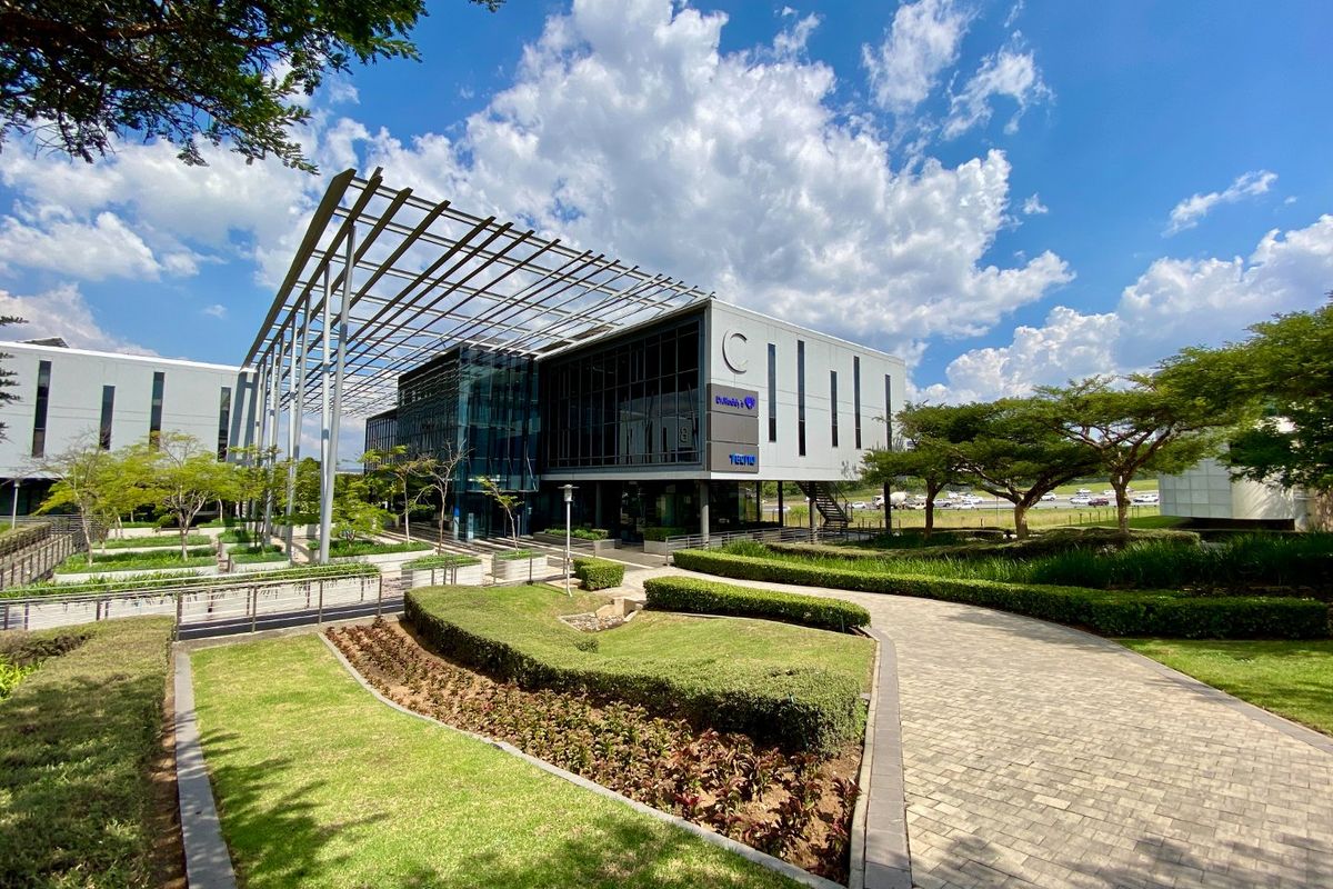 Modern commercial office building featuring a glass facade, steel pergola structure, and well-maintained landscaped gardens with paved walkways.