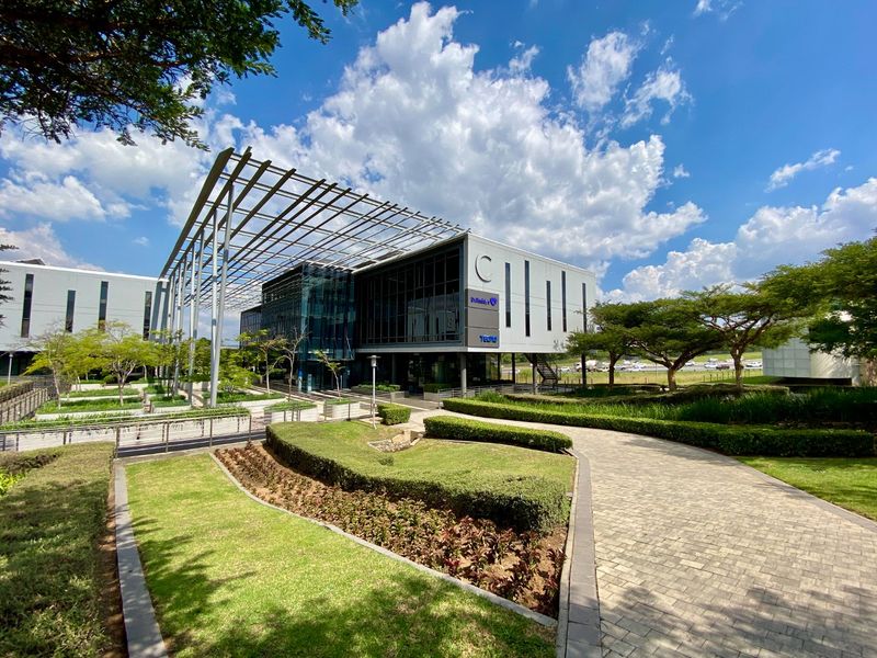 Modern commercial office building featuring a glass facade, steel pergola structure, and well-maintained landscaped gardens with paved walkways.