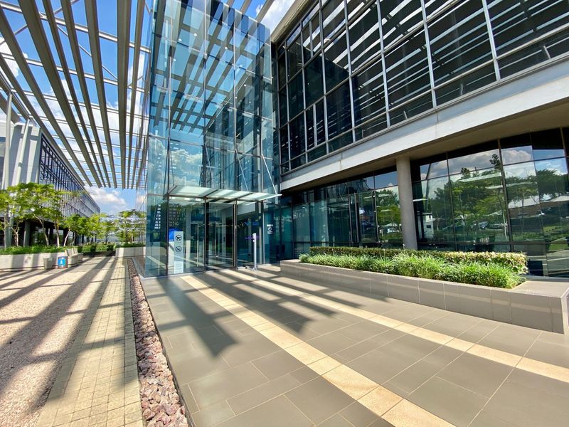 Modern commercial building entrance featuring a glass facade, metal louvre canopy, and paved pedestrian walkway with integrated landscaping.