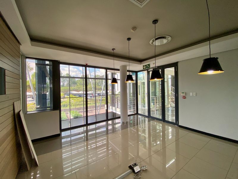 Modern, bright office space featuring large floor-to-ceiling windows, polished porcelain tile flooring, and contemporary pendant lighting in a professional commercial setting.