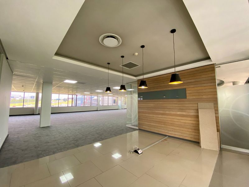 Spacious open-plan commercial office area featuring a mix of carpet and tile flooring, timber wall accents, and modern pendant lighting.