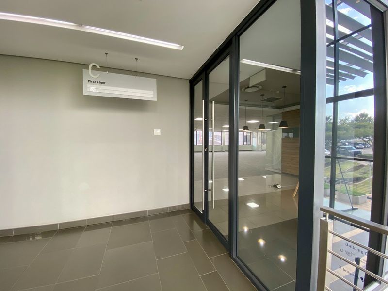 Modern commercial building entrance lobby featuring glass sliding doors, tiled flooring, and clear directional signage leading to the first floor office space.