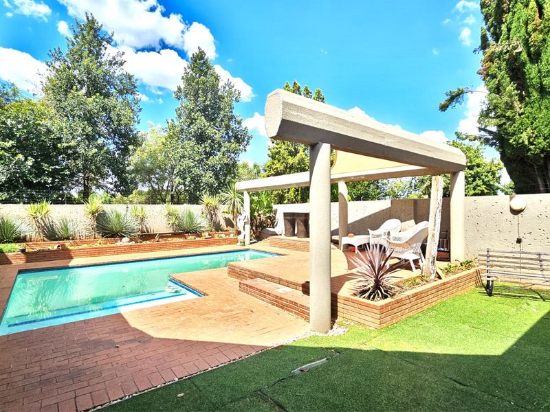 Outdoor pool area featuring a swimming pool, brick paving, a built-in fireplace, and a pergola structure set within a landscaped garden.