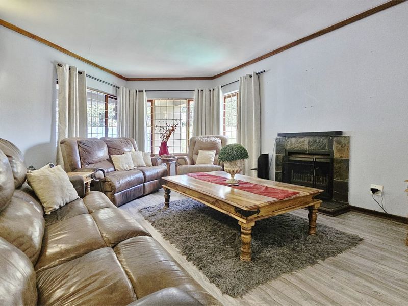 A comfortable living room featuring a stone-clad fireplace, bay windows, and laminate flooring, offering a cozy and functional space for relaxation.