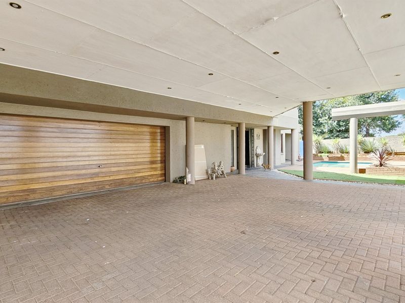 Spacious covered parking area featuring a timber garage door, paved flooring, and recessed lighting, with direct access to the outdoor pool and garden area.