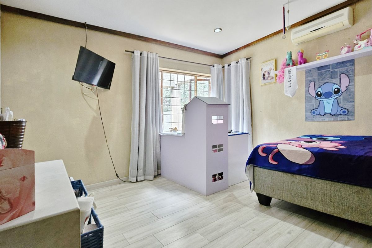 A bedroom featuring light-toned laminate flooring, a split-system air conditioner, and a window with security bars.