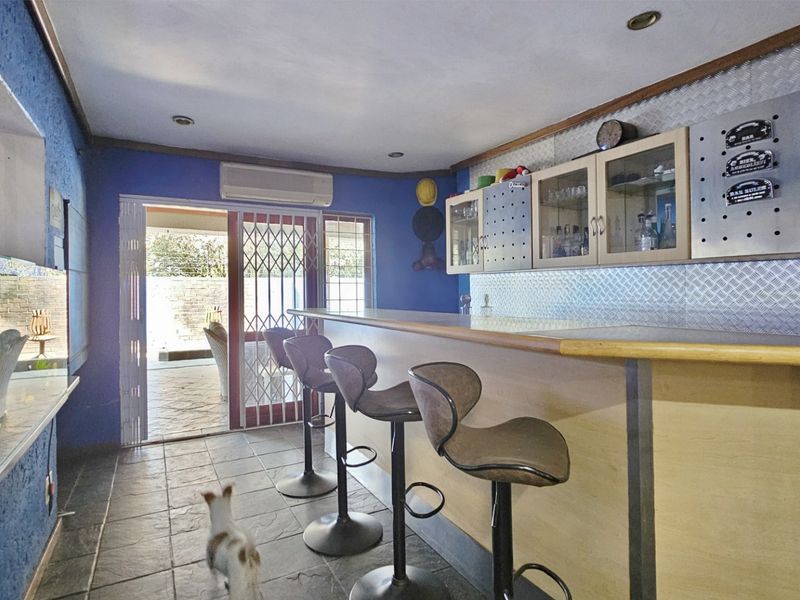 A dedicated bar area featuring a built-in counter, wall-mounted cabinetry, metal splashback, and direct access to an outdoor patio through a security gate.