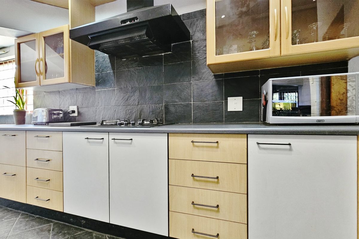 A functional kitchen featuring light wood and white cabinetry, a dark slate tile backsplash, gas hob, and integrated wine storage.