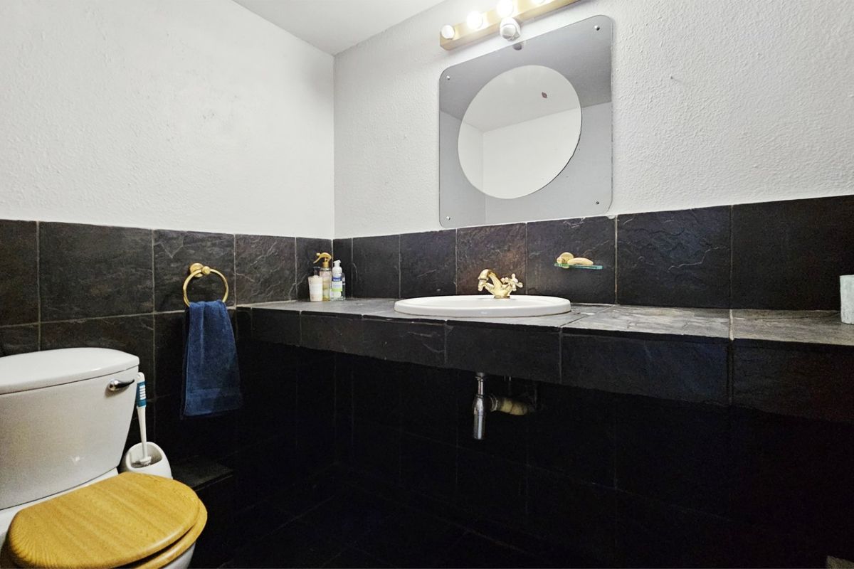 A compact bathroom featuring a slate-tiled vanity with a drop-in sink, brass fixtures, and a wall-mounted mirror.