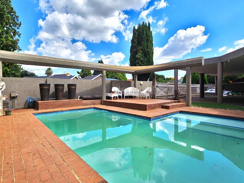 Outdoor pool area featuring a swimming pool, raised brick deck, and a concrete pergola structure, set within a private garden space.