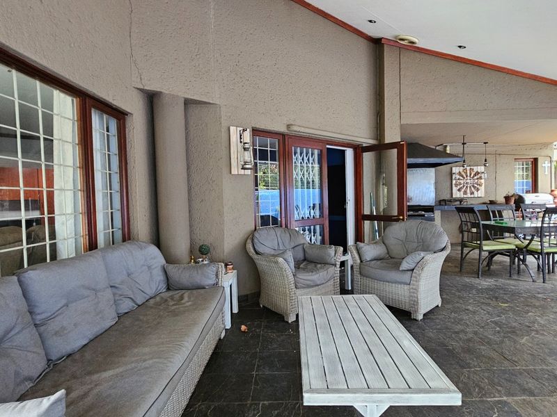 Spacious covered patio featuring a built-in braai, tiled flooring, and direct access to the interior through timber-framed glass doors.