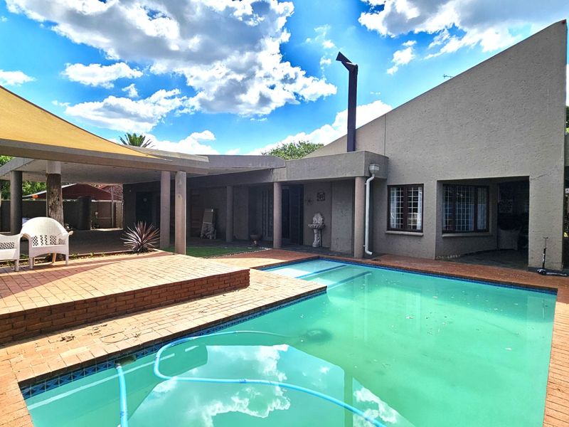 Outdoor pool area featuring a swimming pool, brick paved surround, and a covered patio with a shade sail.