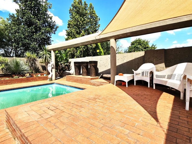 Outdoor pool area featuring brick paving, a shade sail, and a concrete retaining wall, providing a functional space for relaxation and entertainment.