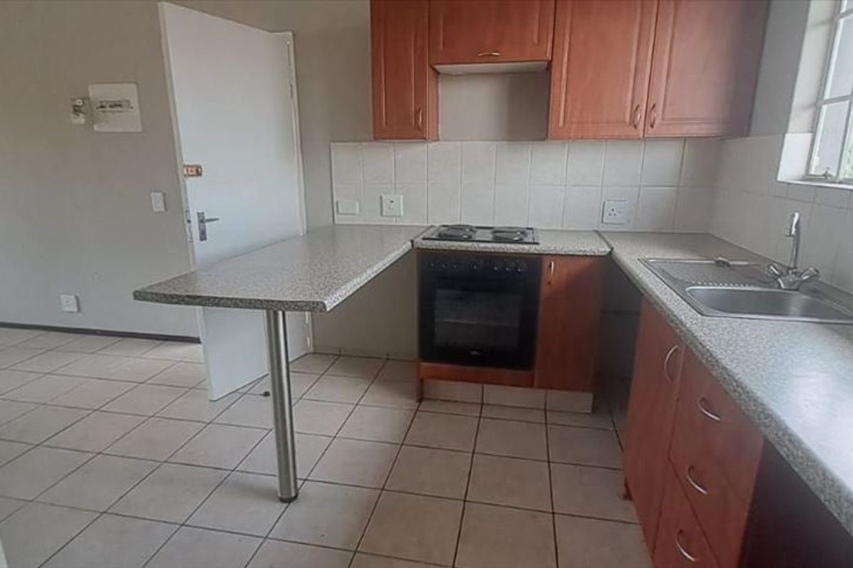 A functional kitchen featuring built-in wooden cabinetry, laminate countertops, an integrated oven and hob, and tiled flooring, offering a clean and practical workspace.