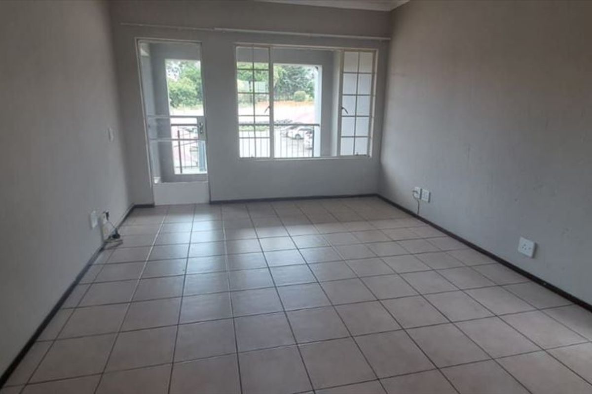 An empty, tiled living room featuring neutral walls, large windows, and a security gate leading to an outdoor area.