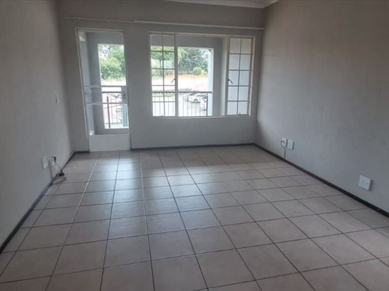 An empty, tiled living room featuring neutral walls, large windows, and a security gate leading to an outdoor area.