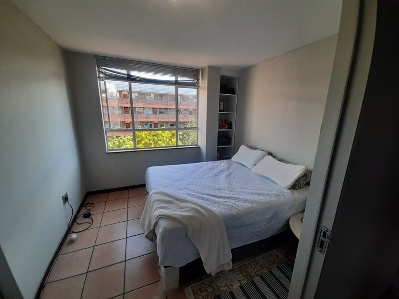 A functional bedroom featuring tiled flooring, built-in shelving, and a large window providing natural light and an urban view.