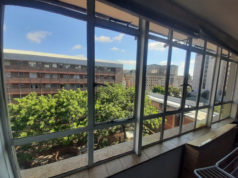An elevated view from an apartment window overlooking surrounding urban buildings and mature trees.
