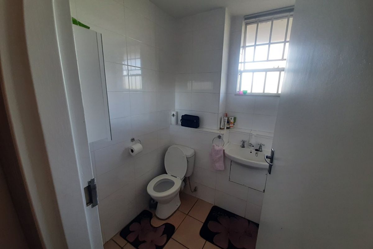 A compact bathroom featuring tiled walls and flooring, a standard toilet, and a wall-mounted basin with security bars on the window.