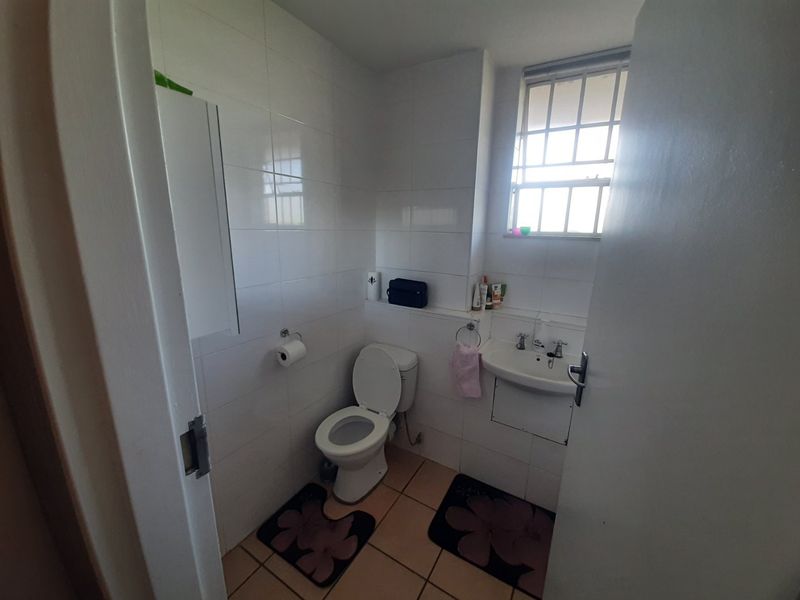 A compact bathroom featuring tiled walls and flooring, a standard toilet, and a wall-mounted basin with security bars on the window.
