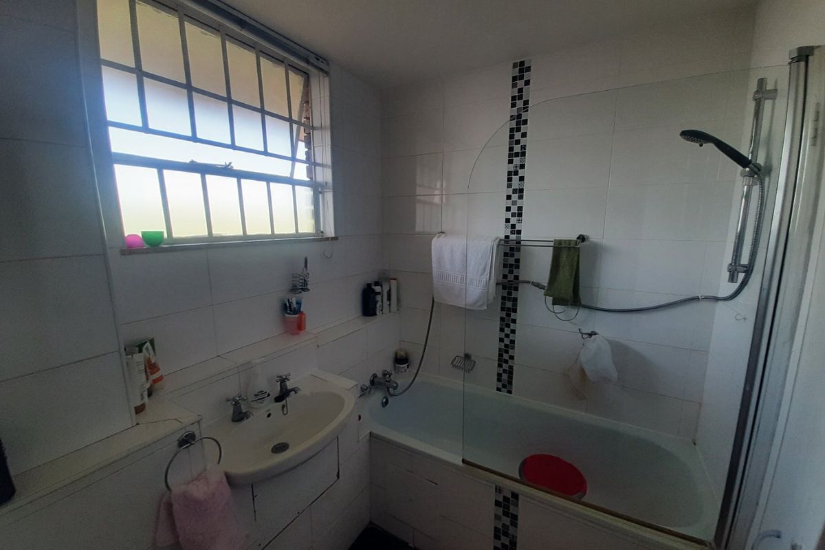 A functional bathroom featuring a bathtub with an integrated shower, glass screen, and white wall tiling with decorative mosaic accents.