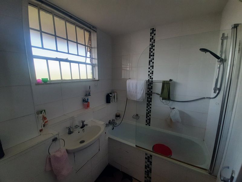 A functional bathroom featuring a bathtub with an integrated shower, glass screen, and white wall tiling with decorative mosaic accents.