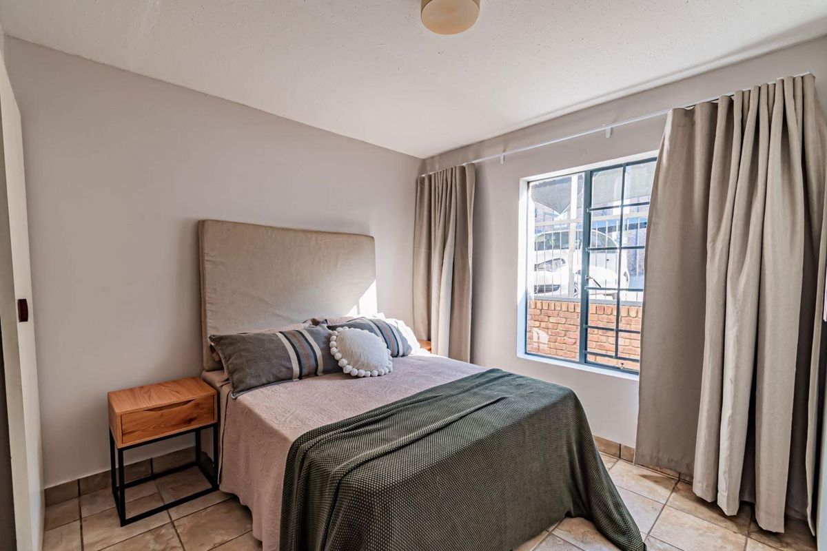 A cozy bedroom featuring tiled flooring and a window fitted with security bars, providing natural light and a view of the exterior.
