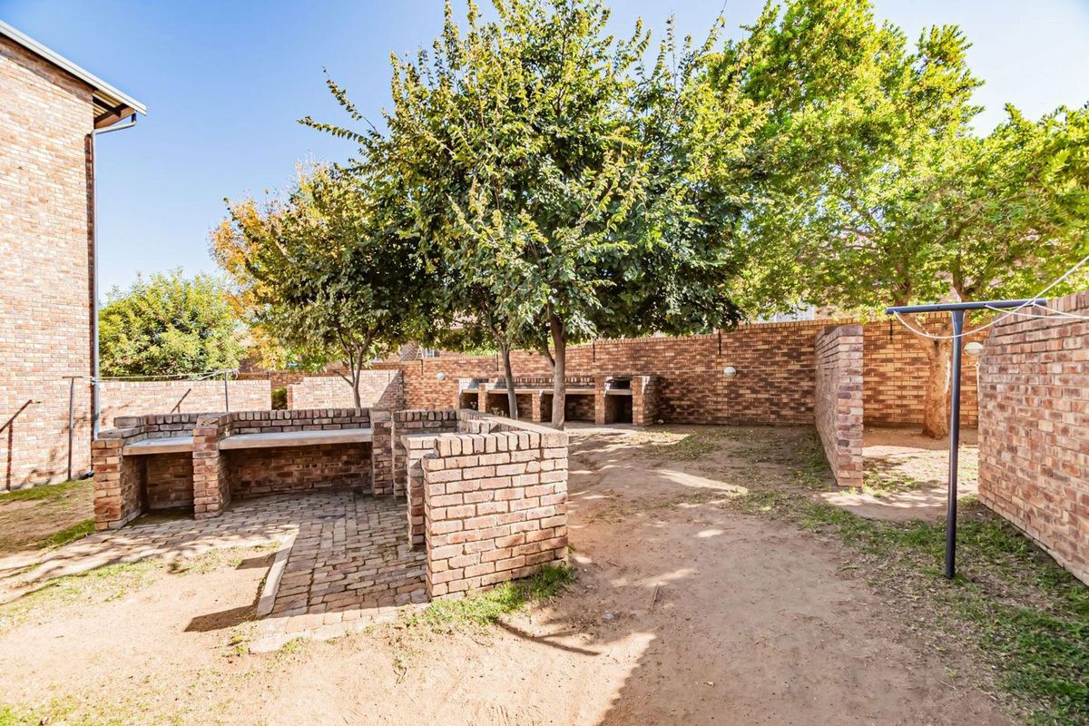 A rear outdoor area featuring a brick-built braai station, paved sections, and established trees enclosed by a brick boundary wall.