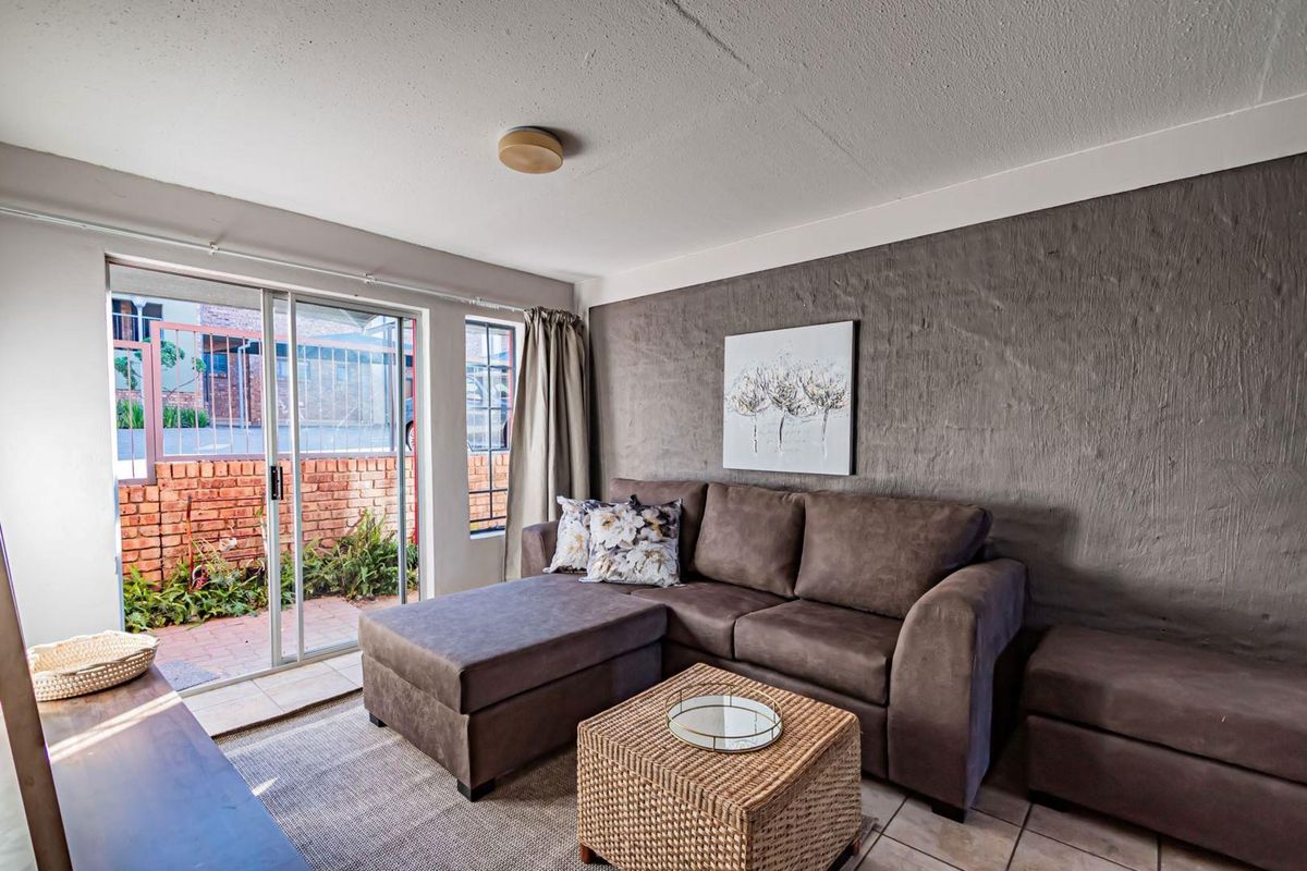 A living room featuring a textured accent wall, tiled flooring, and a sliding glass door providing access to an outdoor patio area.