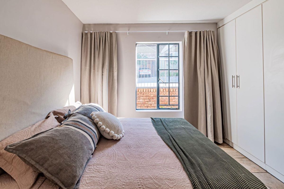 A well-maintained bedroom featuring built-in cupboards and a steel-framed window, offering a clean and functional living space.