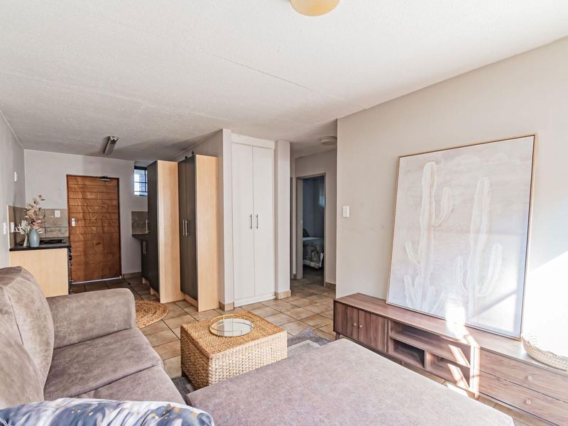 Open plan living area featuring tiled flooring, built-in storage cupboards, and a solid wood entrance door, providing a functional and connected layout.