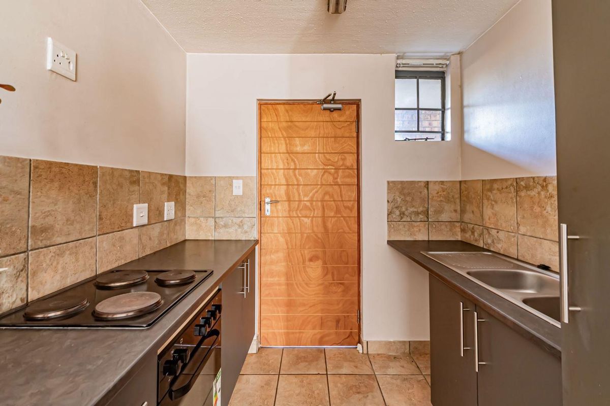 Compact kitchen featuring built-in cabinetry, laminate countertops, an electric hob, oven, and a stainless steel double sink with tiled backsplash and flooring.