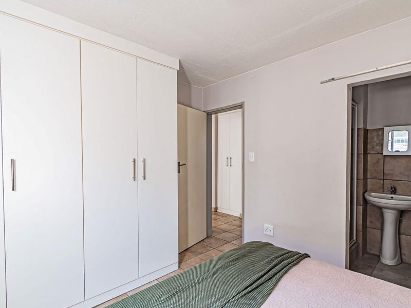 A bedroom featuring built-in cupboards and an adjoining en-suite bathroom with a pedestal basin and tiled flooring.