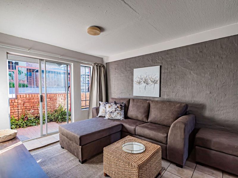 A living room featuring a textured accent wall, tiled flooring, and a sliding glass door providing access to an outdoor patio area.