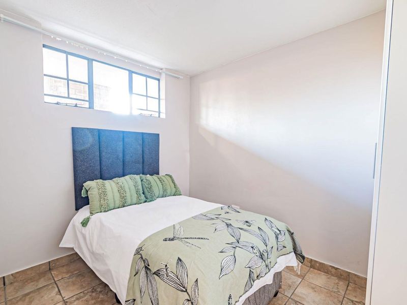 A compact bedroom featuring tiled flooring, a built-in wardrobe, and a multi-pane window providing natural light.