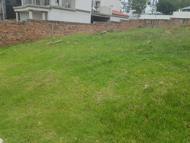 A vacant residential plot featuring a grass lawn and a brick boundary wall, offering a clear space for potential development.