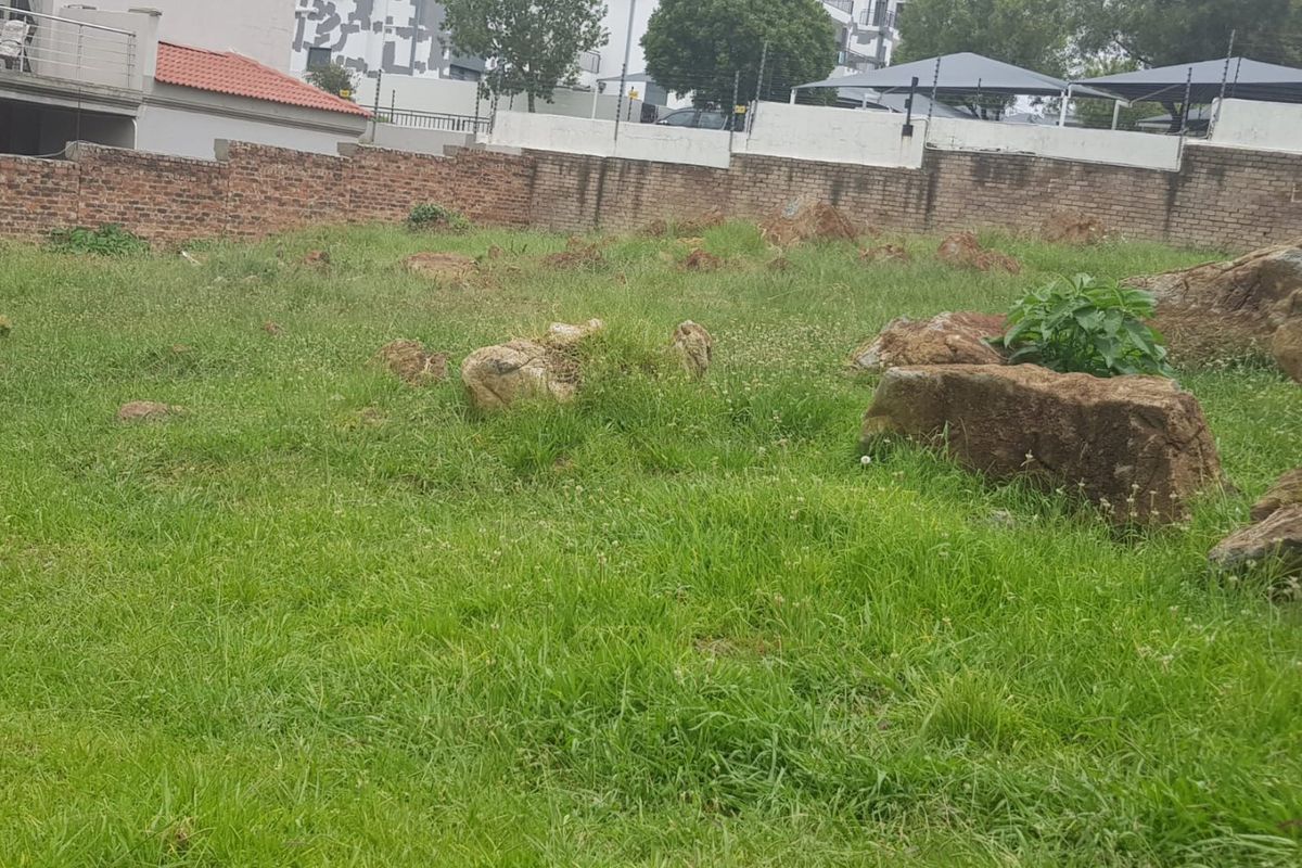 A vacant residential plot featuring natural rock outcrops, enclosed by a brick boundary wall with electric fencing.