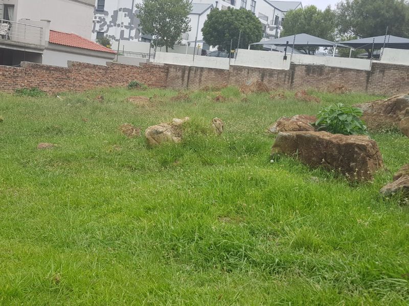 A vacant residential plot featuring natural rock outcrops, enclosed by a brick boundary wall with electric fencing.