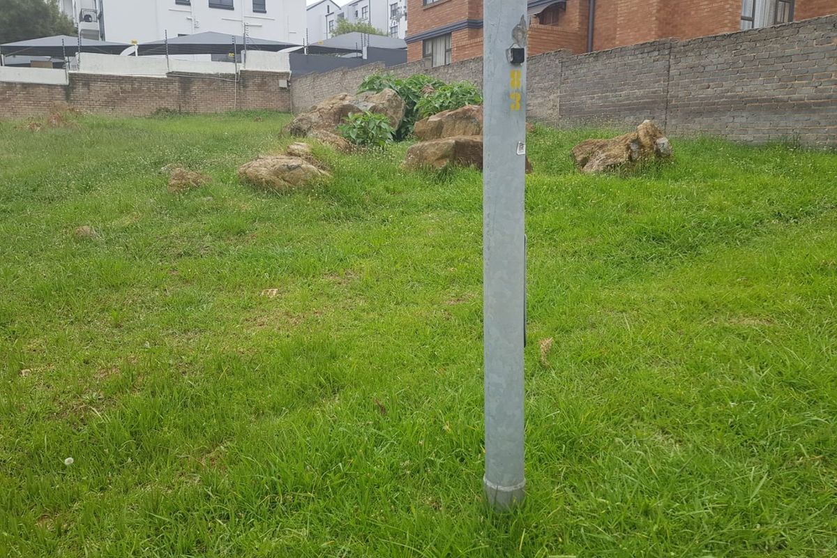 A vacant residential plot featuring a grassed area, natural rock formations, and a perimeter brick boundary wall.
