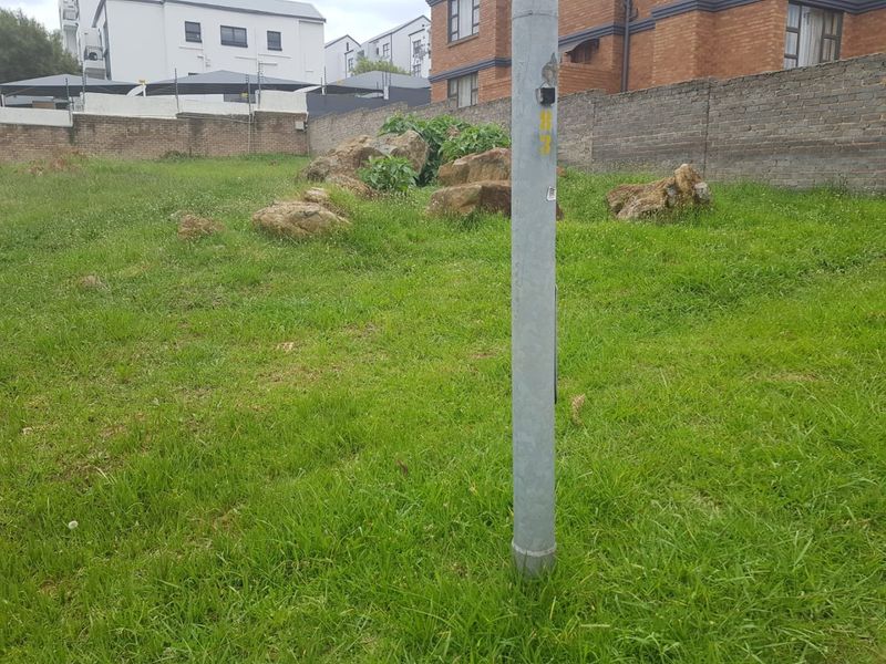 A vacant residential plot featuring a grassed area, natural rock formations, and a perimeter brick boundary wall.