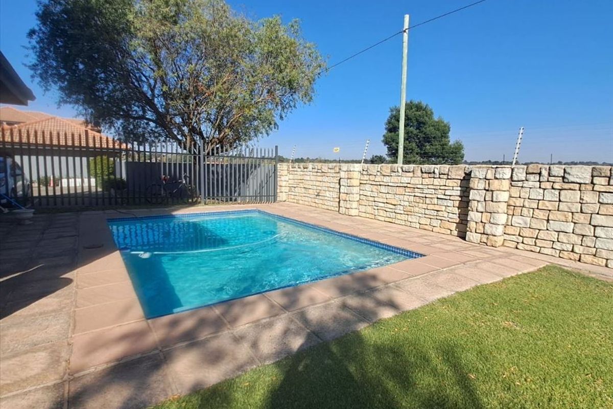 A private swimming pool area featuring a paved surround, manicured lawn, and a decorative stone boundary wall.