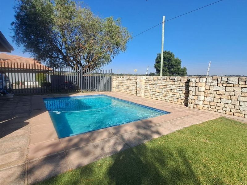 A private swimming pool area featuring a paved surround, manicured lawn, and a decorative stone boundary wall.