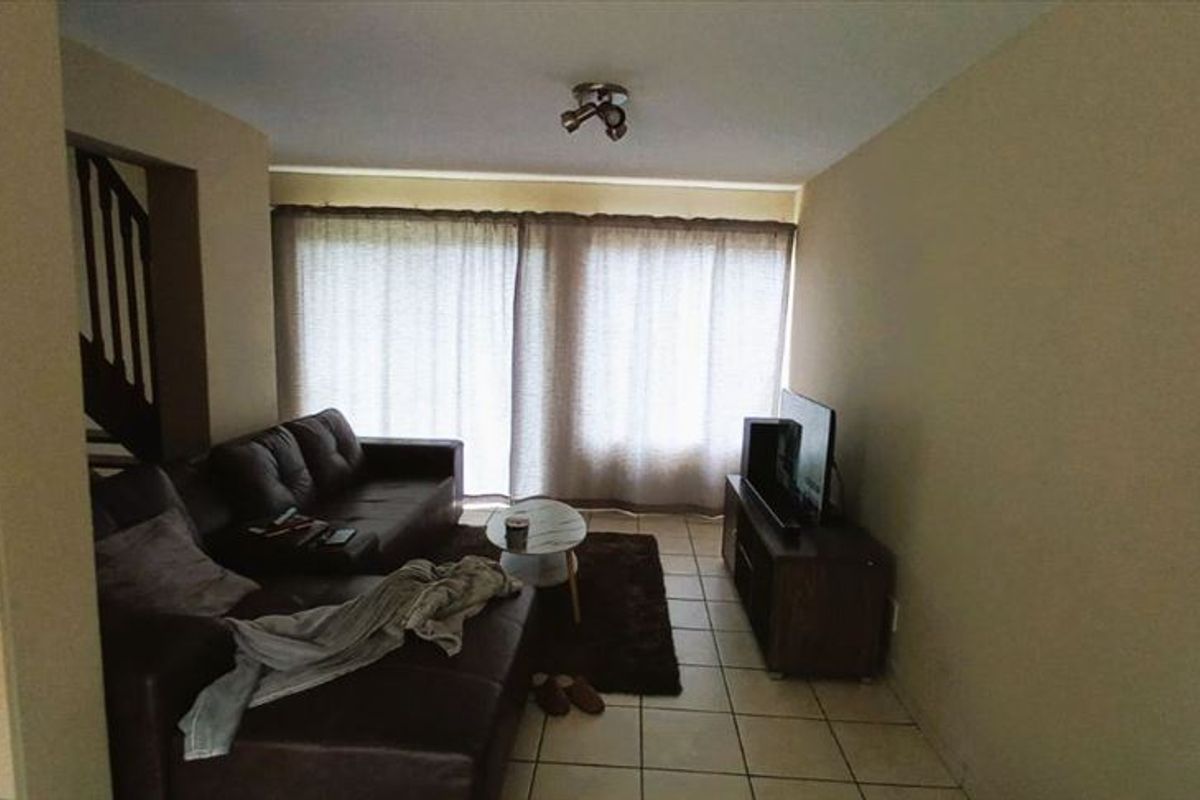 A living room featuring tiled flooring and large sliding glass doors that provide natural light, with an adjacent staircase leading to the upper level.