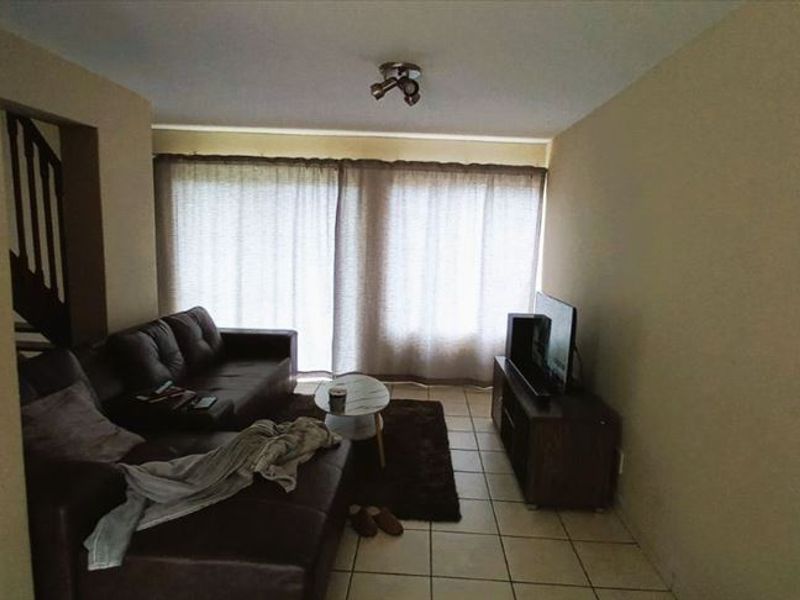 A living room featuring tiled flooring and large sliding glass doors that provide natural light, with an adjacent staircase leading to the upper level.
