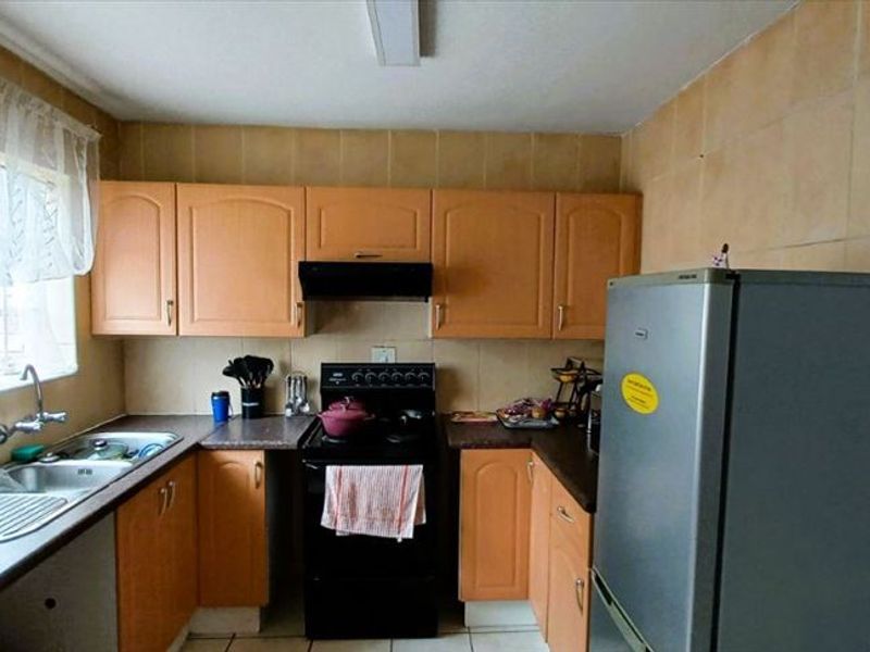 A functional kitchen featuring laminate cabinetry, tiled splashbacks, and a stainless steel sink, offering a practical layout with potential for modern cosmetic updates.
